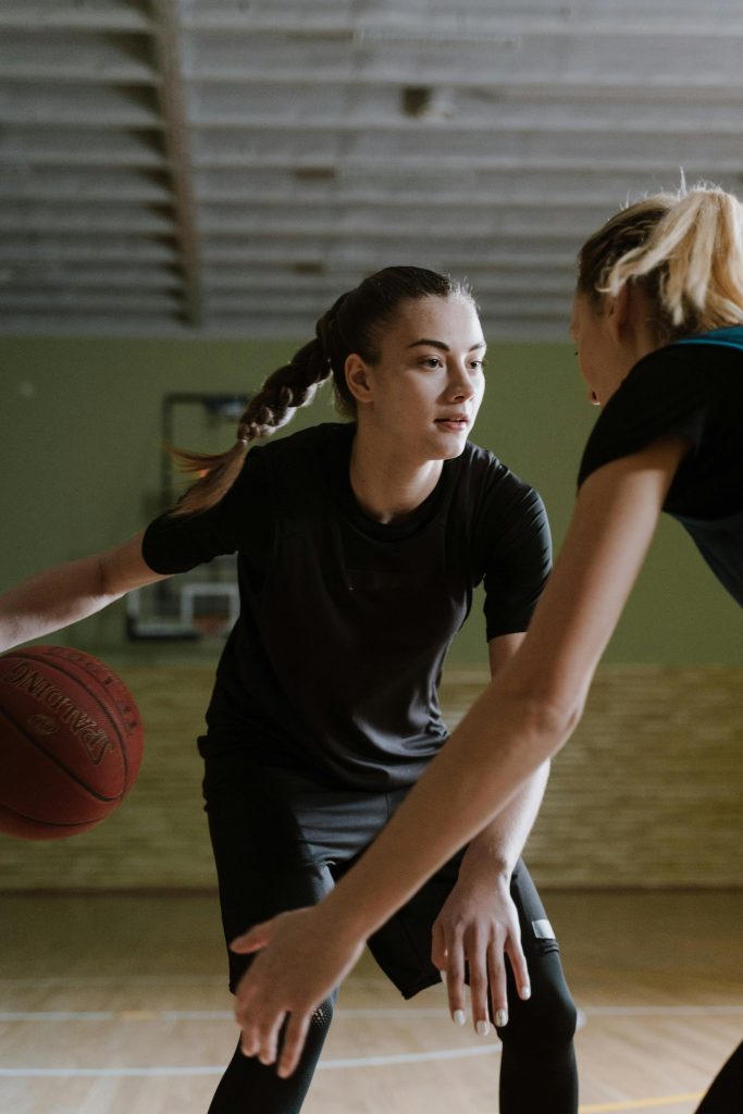 Two women intensely playing basketball indoors on a court, showcasing determination and athleticism.